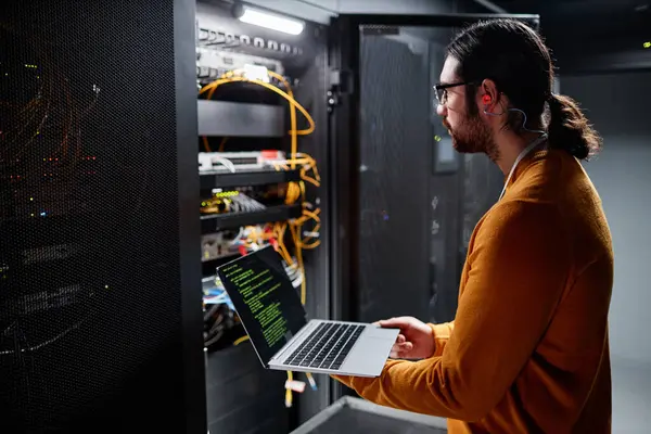 Side view portrait of bearded IT engineer using laptop while setting up network in server room