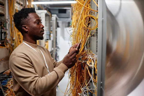 Side view portrait of black man as system administrator setting up server and using smartphone