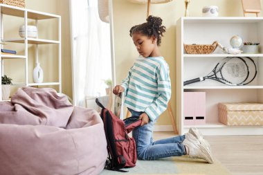 Pembe iç mekan içinde okul için bavul hazırlayan sevimli siyah kız portresi.