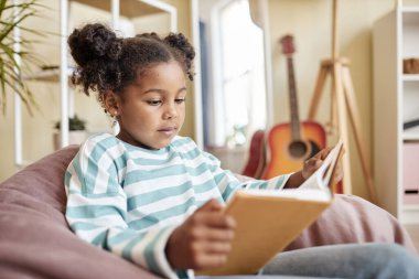 Evde kitap okuyan küçük siyah bir kızın portresi rahat bir koltukta oturup, fotokopi çekiyor.