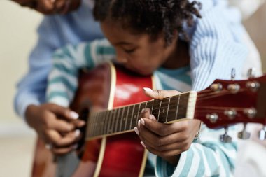 Evinde annesiyle gitar çalan sevimli siyahi kızın samimi yakın plan portresi.