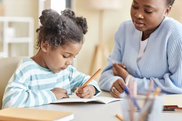 Side view portrait of cute black girl studying with tutor and writing in notebook