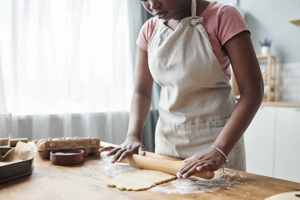 Cropped portrait of black woman baking homemade pastry and rolling dough on wooden kitchen counter, copy space