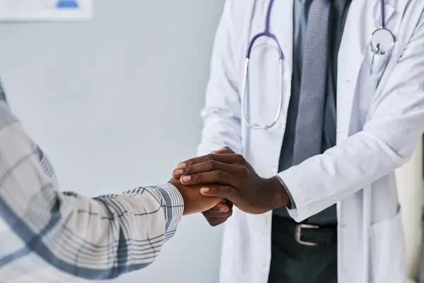 Close up of caring black doctor holding hands with female patient to support and comfort