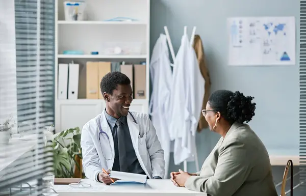 Side view portrait of young black doctor consulting patient in clinic and smiling happily