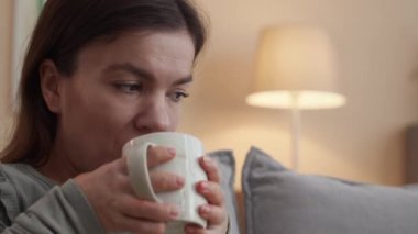 Cüce gibi gülümseyen genç bir kadının oturma odasında rahatça oturup film izlediği ve çay içtiği bir sahne.