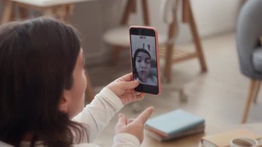 Oturma odasındaki koltukta oturan beyaz tenli genç bir kadının akıllı telefondaki videosunu kaydedip kamerada hikâyelerini paylaştığı orta ölçekli bir fotoğraf.