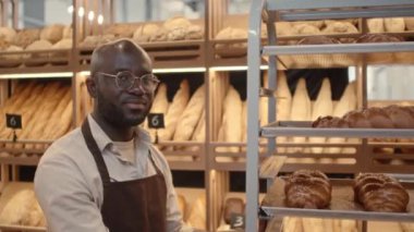Gülümseyen genç Black pastane işçisinin belden yukarı portresi alüminyum tepside taze ekmek somunlarıyla kameraya poz veriyor.