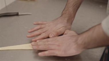 Pastanedeki paslanmaz çelik çalışma masasında hamuru kruvasana saran tanınmayan erkek elleri.