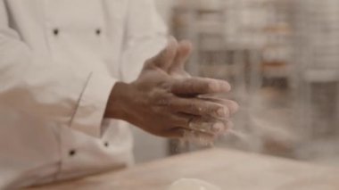 Fırın mutfağında çalışırken güçlü unlu elleriyle ekmek hamuru şekillendiren tanınmayan erkek fırıncının yavaş yavaş yakın çekimi.