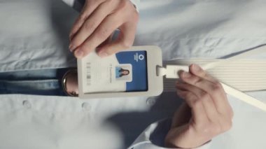 Gözlüklü genç beyaz kadın bilişim koordinatörünün dikey olarak stüdyo portresi. Rozeti boynunda asılı ve gri arka planda dururken kameraya bakıyor.