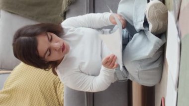 Oturma odasındaki halıda oturan beyaz kadının dikey hali. Ofiste evrak ve dizüstü bilgisayar yığınları arasında oturuyor.