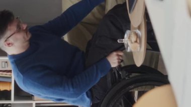 Kafkasyalı engelli bir gencin dikey pozu. Kendini koltuktan kaldırma çabası ve modern rahat ofiste çalışma gününde tekerlekli sandalyeye oturma çabası.