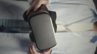 Açık mavi tişörtlü, ayakta duran ve titreyen siyah vr kulaklıklı tanımadığımız birinin dikey görüntüsü.