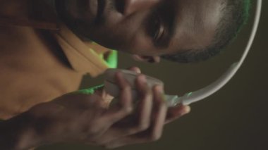 Dikey yarım yüz, genç Afrikalı Amerikalı bir adamın kablosuz beyaz kulaklık takarken kameraya baktığı ağır ağır ağır portresi.