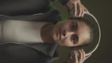 Kafkasyalı gri kapüşonlu bir kızın dikey belden yukarı portresi kablosuz kulaklık takıyor ve karanlık stüdyo arka planında dikilip kameraya bakarken kaputu çekiyor.