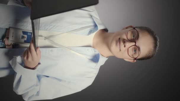 年轻白种人女程序员头戴眼镜和身份证 头戴灰色背景的敞开式笔记本电脑 站在镜头前微笑的垂直媒体工作室肖像 — 图库视频影像