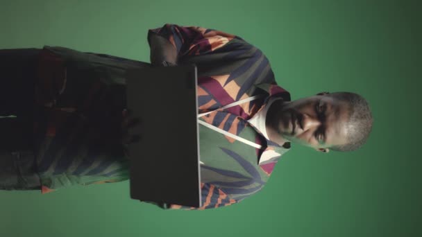 背景为深绿色的带笔记本电脑的年轻黑人男子的垂直媒体肖像 — 图库视频影像