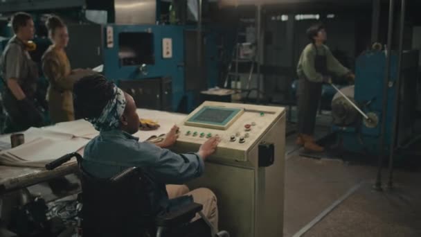 バックビュー ブルーデニムシャツとバンダナを着用した若い黒人女性のメディアショット 他の多様な女性との工場で働いている間 彼女のヘッドオペレーティングマシン機器に — ストック動画