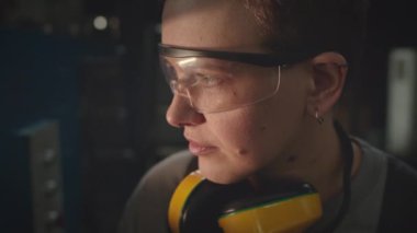 Güvenlik gözlüğü ve kulaklık takmış, fabrikadaki endüstriyel ekipmanlara bakan Kafkas kadın makine bakım işçisinin basit bir resmi.
