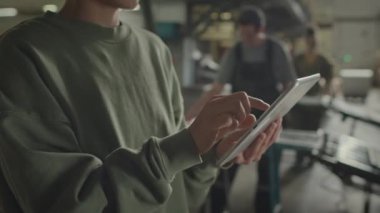 Tanımlanamayan fabrika müdürünün dijital tablet üzerinde çalışırken çekilmiş görüntüsü bulanık arka planda çalışan çalışanlarla birlikte.