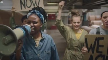 Dört güçlü çok ırklı kadının, grev sırasında sanayi fabrikası boyunca karton pankartlarla yürürken adalet ve ağızlık talep ederken orta boy bir fotoğrafı.
