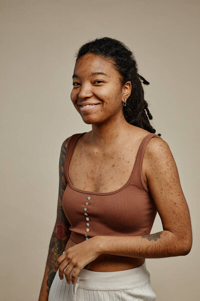 Vertical waist up portrait of expressive ethnic young woman with tattoos looking at camera and smiling candidly
