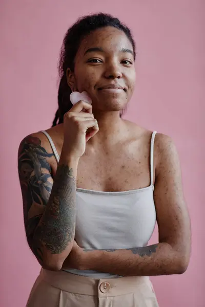 用面部按摩器对着粉红微笑 对有粉刺疤痕的年轻黑人妇女的垂直肖像 — 图库照片