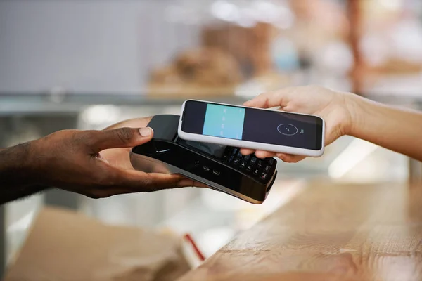 Hand of customer using banking app when paying for purchase in bakery