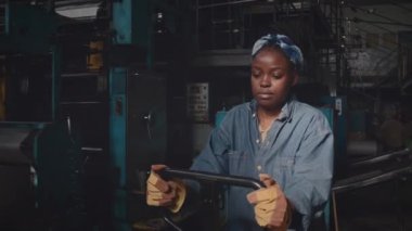 Siyah kadın fabrika işçisinin nalbur makineleri arasında el arabası çekerken belini kaldır.