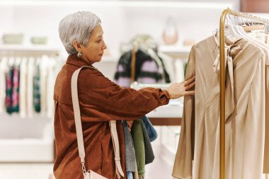 Son sınıf öğrencisi bir kadının alışveriş merkezindeki lüks mağazalarda kıyafetlerini karıştırması.