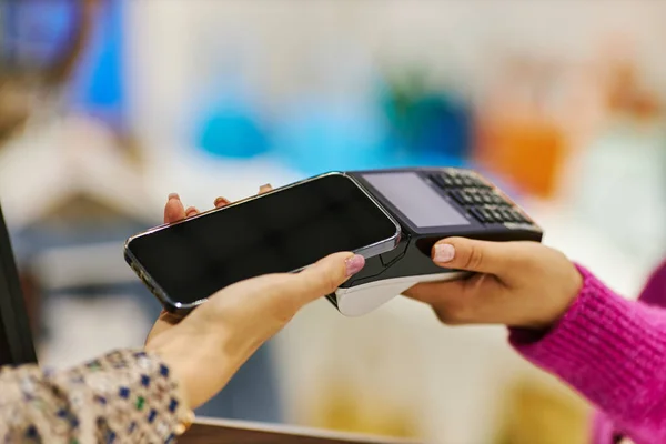 Side view closeup of woman paying via smartphone NFC in shopping mall, copy space
