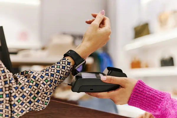 Side view close up of young woman paying via smartwatch in boutique or shopping mall, copy space