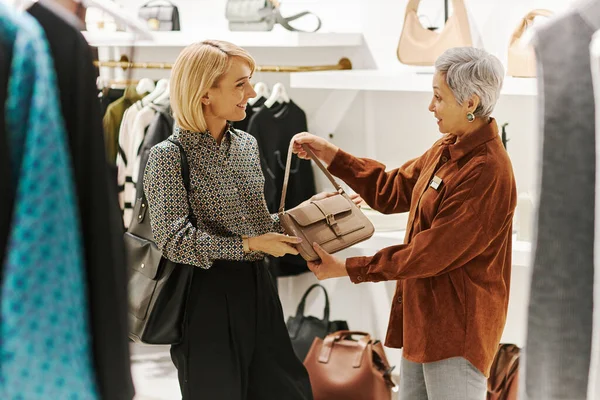 Adult mother and daughter enjoying shopping together and choosing bags at luxury boutique