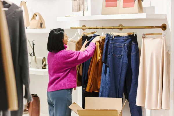 Back view of young woman managing clothing boutique in shopping mall, copy space