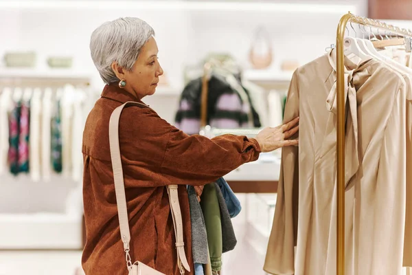 Side view of senior woman browsing clothes on racks in luxury boutique at shopping mall