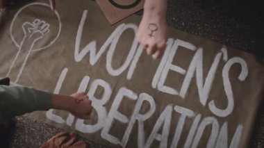 Arka planda dört farklı aktivist kadının el yapımı Kadın Kurtuluş bayrağının üzerinde feminist bir tabela olan yumruklarını üst üste koyması.