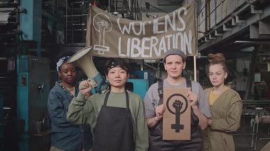 İçerideki göstermelik poster ve ağızlık ile kameraya poz veren feminist hareketi destekleyen dört kadın bitki işçisinin orta yavaş portresi.