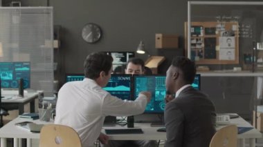 Ofiste birlikte çalışırken ağ bilgisayar programında veri bilgilerini tartışan üç çoklu etnik erkek siber güvenlik görevlisinin orta boy görüntüsü.