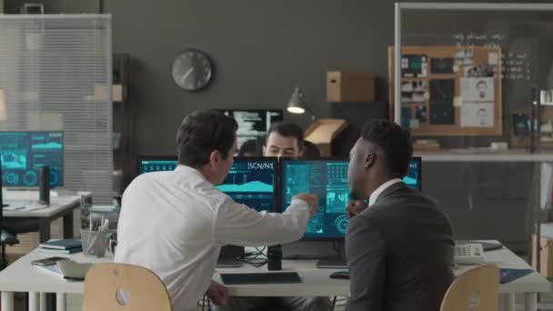 オフィスの共同作業中にネットワークコンピュータプログラムのデータ情報を議論する3人の多民族男性サイバーセキュリティ担当者の中型ショット — ストック動画