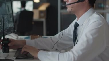 Beyaz erkek siber güvenlik çalışanı mobese kameralarını izliyor ve ofiste çalışırken telsizle bilgi aktarıyor.