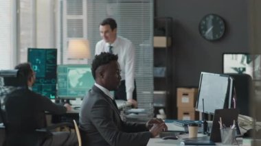 Ofiste çalışırken güvenlik kameralarını ve gizli ağ veri programlarını izleyen profesyonel siber güvenlik ajanlarından oluşan çok ırklı erkek ekibinin orta boy görüntüsü.