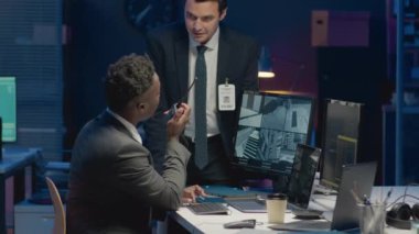 CCTV kameralarını izleyen ve geceleri ofiste çalışırken telsizle bilgi aktaran iki farklı erkek siber güvenlik uzmanının orta boy görüntüsü.