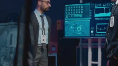 Formalite icabı giyinmiş iki farklı erkek siber güvenlik görevlisinin ekrandaki teknik verilere bakarken ve karanlık ofiste tartışırken orta boy görüntüsü.