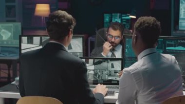 Çoklu etnik çeşitliliğe sahip siber güvenlik ajanları, bilgisayarları başında otururken birden fazla CCTV kamerası ve ağ programları görüntülenir ve gece ofisinde iş birliği yaparken tartışırlar.