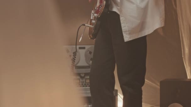 ポリエチレンシートで満たされたスモーキーミュージックスタジオでエレクトリックギターを演奏する若い白人男性ギタリストのチルトアップスローモショットと床のリールトゥーリールテープレコーダー — ストック動画