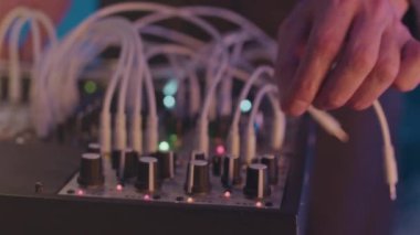 Gece kulübünde neon sahnede çalarken genç beyaz erkek dj 'lerin ses kablolarını modüler sentetiğe takması.