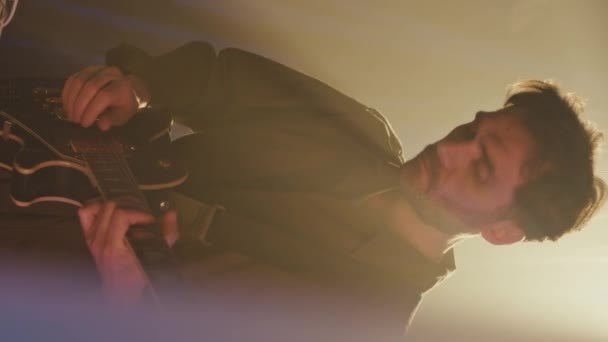 白人青年嬉皮士男子在黑暗霓虹灯演播室练习电吉他时使用模块化合成器时的垂直中等速度 — 图库视频影像