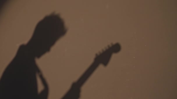 从无法辨认的男歌手弹奏电吉他的投影机灯光看墙上的黑暗轮廓 — 图库视频影像