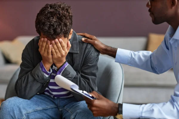 School psychologist reassuring teenage boy crying when talking about his problems